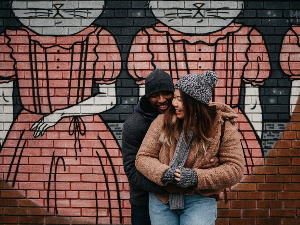 moment de complicité entre deux amoureux devant une fresque murale colorée lors d'une séance photo de couple en hiver