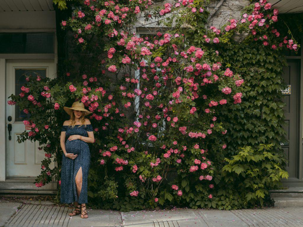 future maman caressant son ventre rond devant un magnifique rosier lors d'un shooting photo grossesse lifestyle en extérieur à Marseille