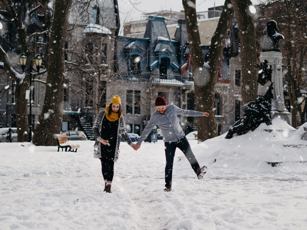 couple heureux marchant sous la neige pendant une séance photo de grossesse lifestyle en hiver