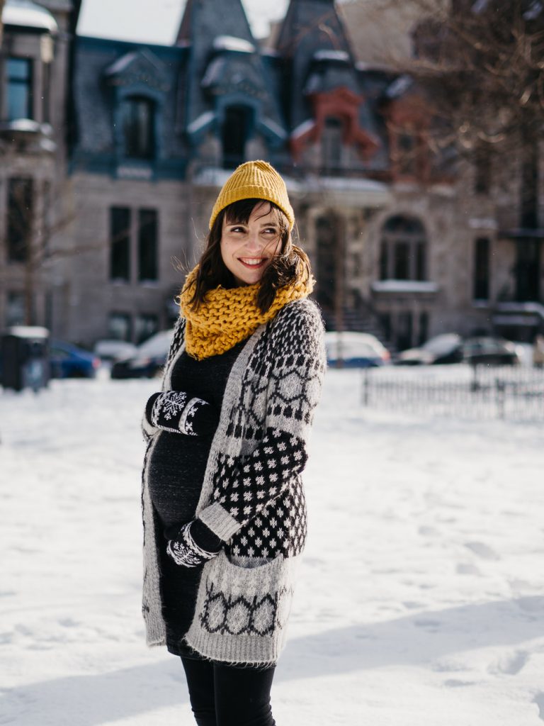 future maman souriante caressant son ventre rond pendant un shooting photo grossesse lifestyle sous la neige