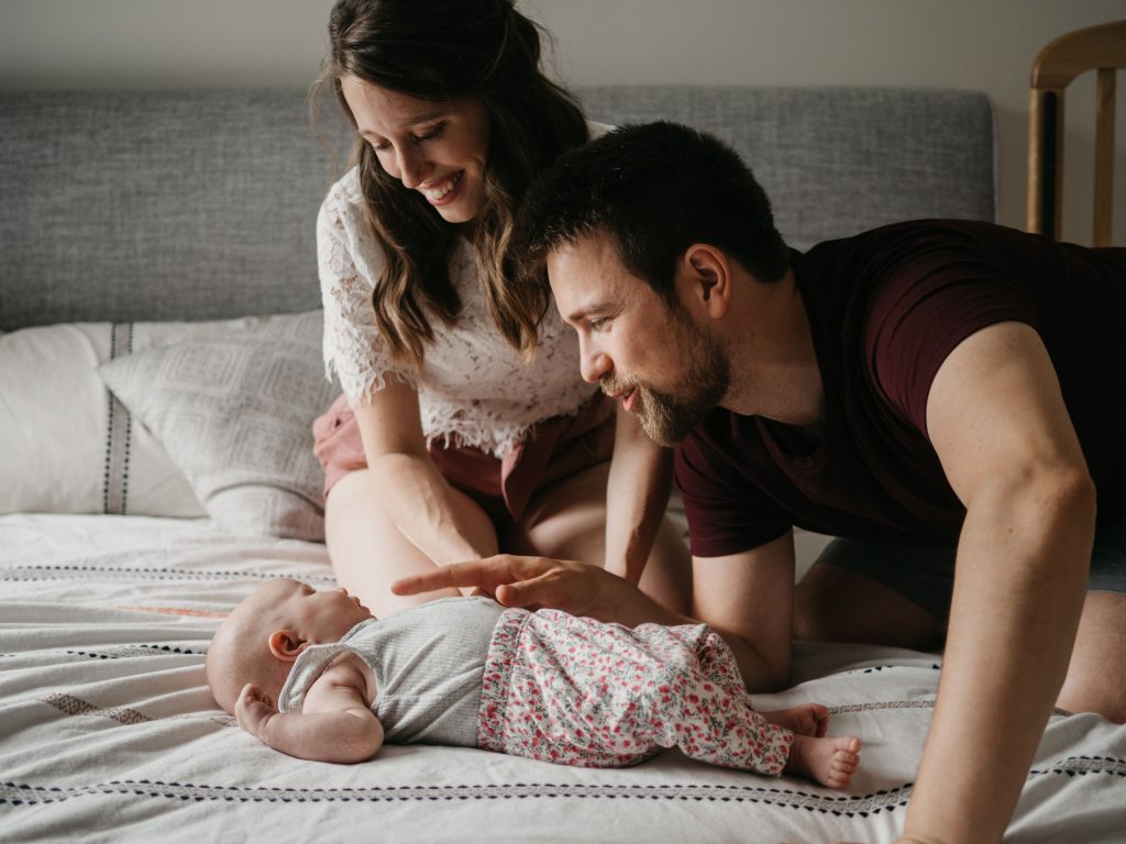 parents regardant tendrement leur bébé sur le lit lors d'une séance photo nouveau-né à domicile à Marseille