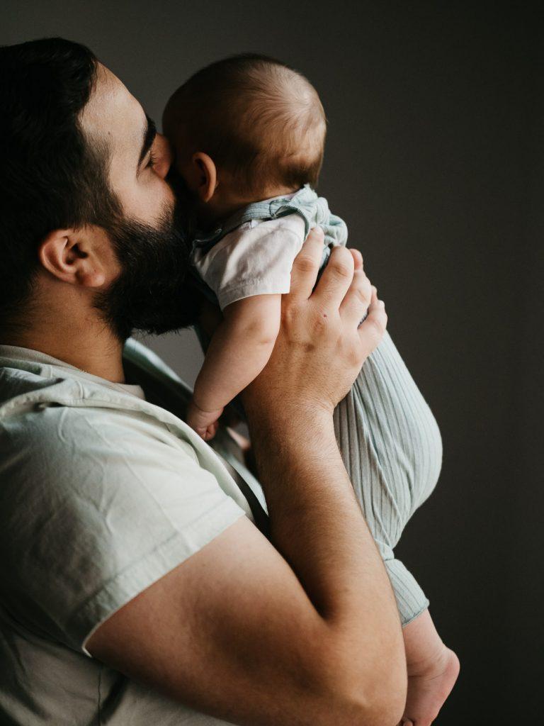 scène de tendresse entre papa et son bébé dans les bras lors d'un shooting photo nouveau-né lifestyle à la maison à Marseille
