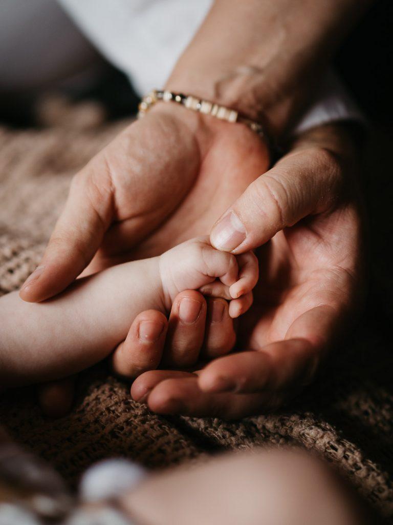 main de bébé dans les mains de ses parents pendant une séance photo à domicile
