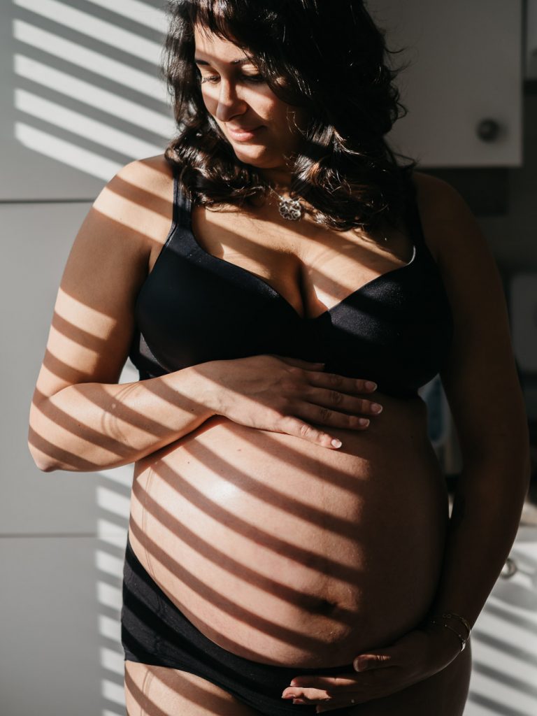 effet d'ombre et de lumière sur une future maman en sous-vêtements caressant son ventre nu de femme lors d'une séance photo de grossesse boudoir à domicile à Marseille