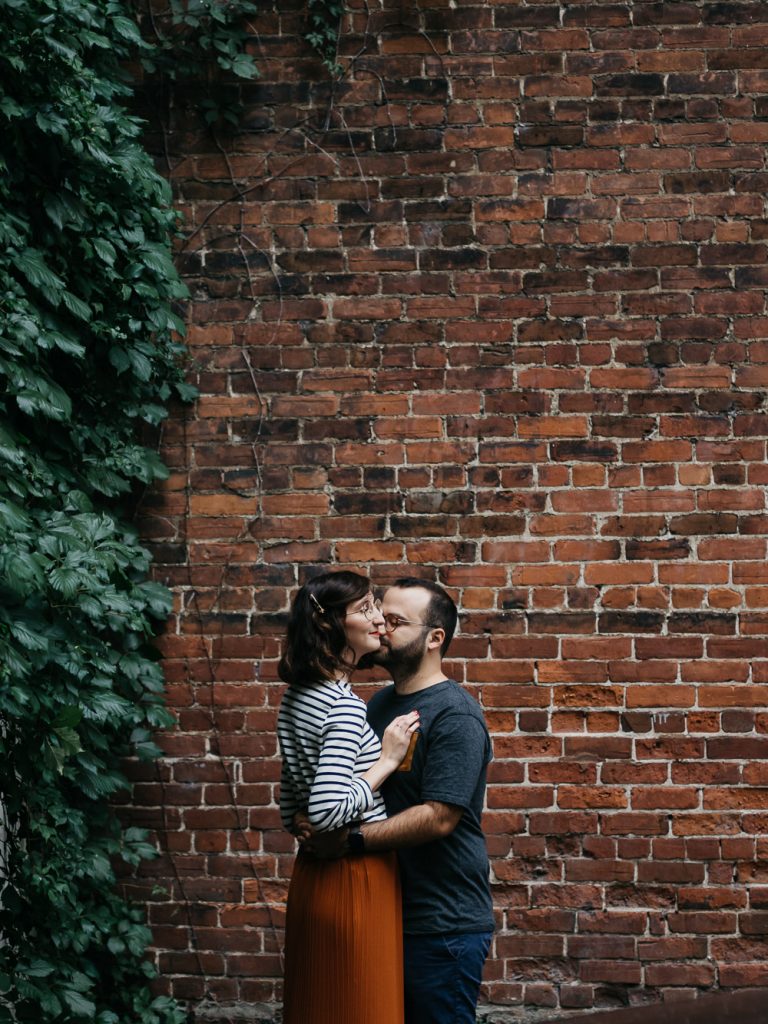 Portrait de couple heureux lors d'une séance photo devant un mur de brique. Instant de tendresse et de complicité