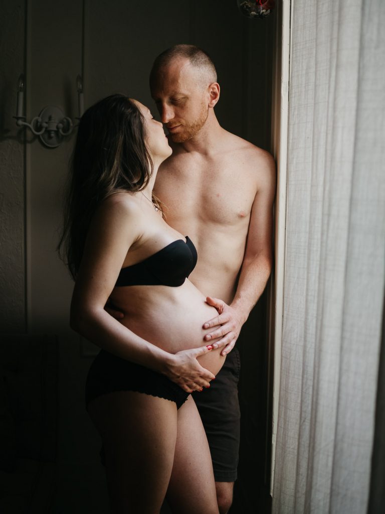 couple en sous vêtements posant lors d'une séance photo de grossesse, la main du papa posée sur le ventre rond de la future maman