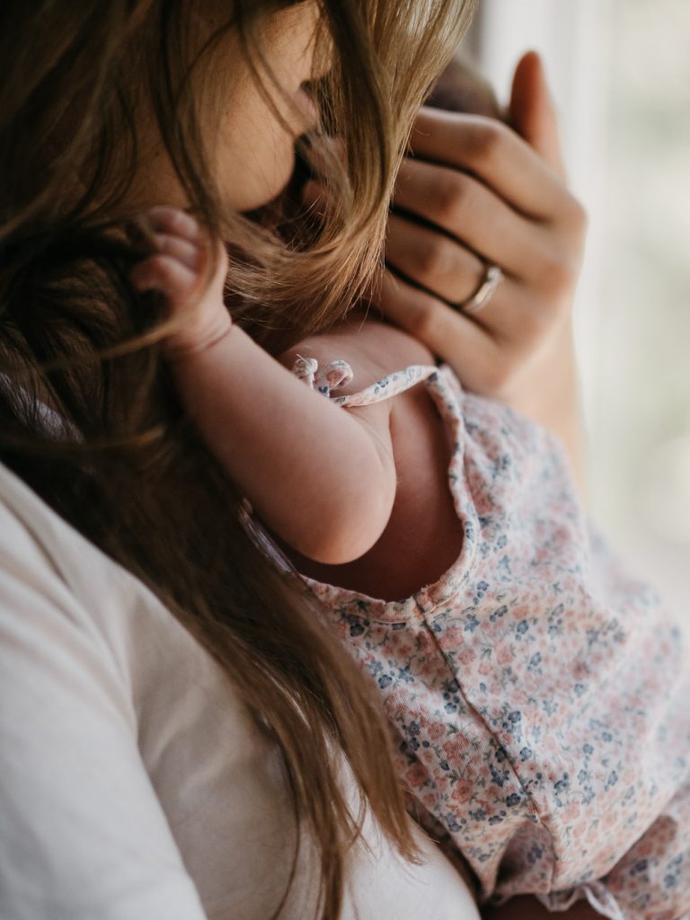 maman berce son bébé dans les bras lors d'un shooting photo nouveau-né lifestyle à la maison à Marseille