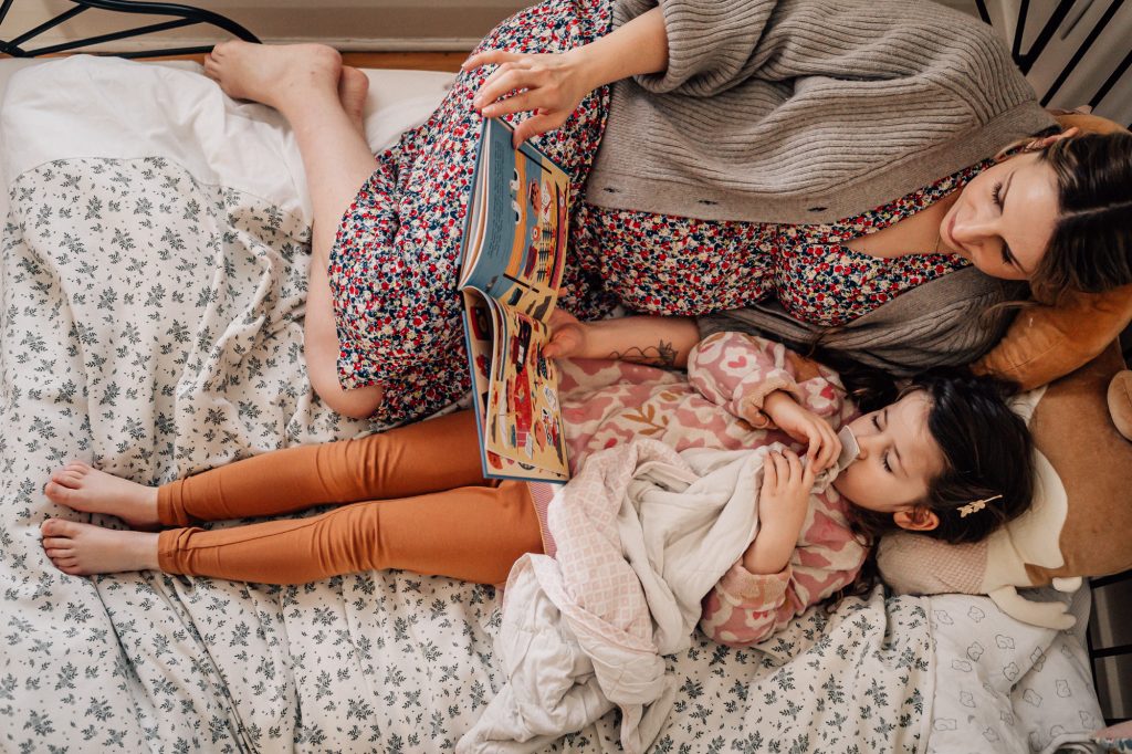 image haute en couleurs et en motifs d'un moment de complicité d'une maman qui lit un livre à sa petite fille sur le lit