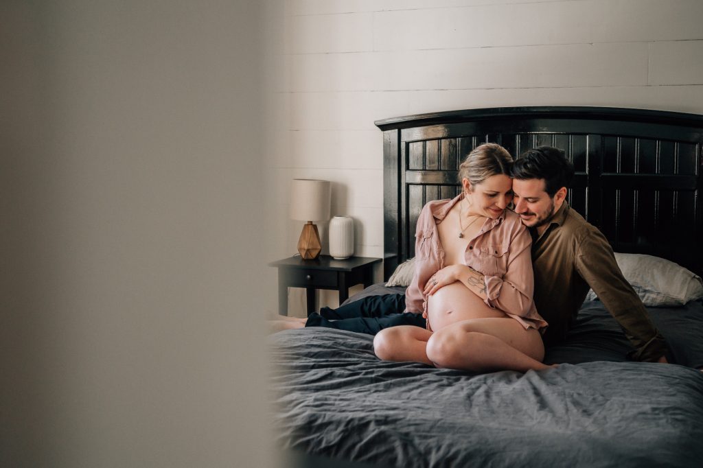 futurs parents complices assis le lit familial, maman dévoile son ventre nu lors d'une séance photo de grossesse à domicile à marseille