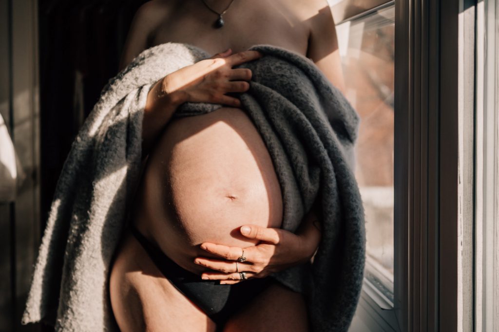 Gros plan sur le ventre d’une femme enceinte enveloppé dans une couverture lors d’une séance photo grossesse en hiver à domicile à Marseille