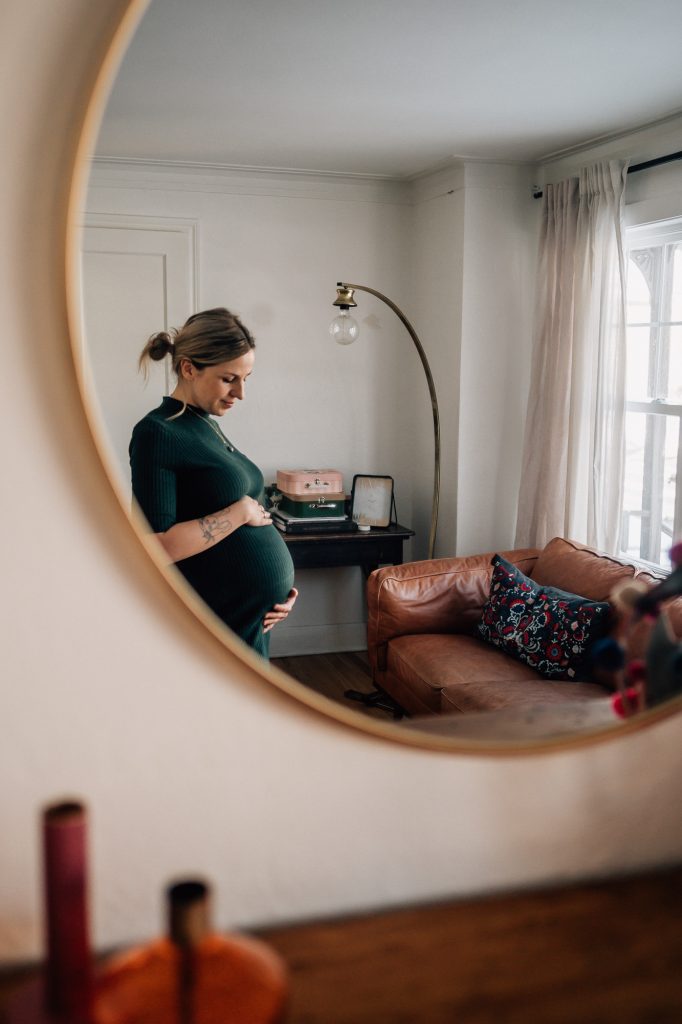 reflet dans le miroir d'une maman caressant son ventre de femme enceinte lors d'une séance photo de grossesse boudoir à domicile à Marseille