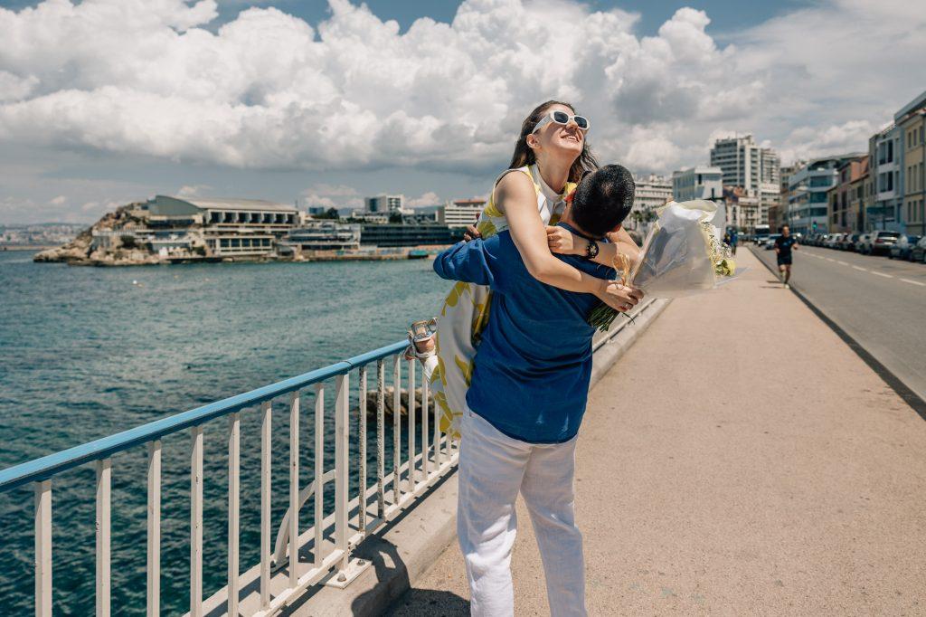 Fiancée heureuse saute dans les bras de son partenaire après une demande en mariage surprise lors d'une séance photo de couple pendant un voyage à Marseille