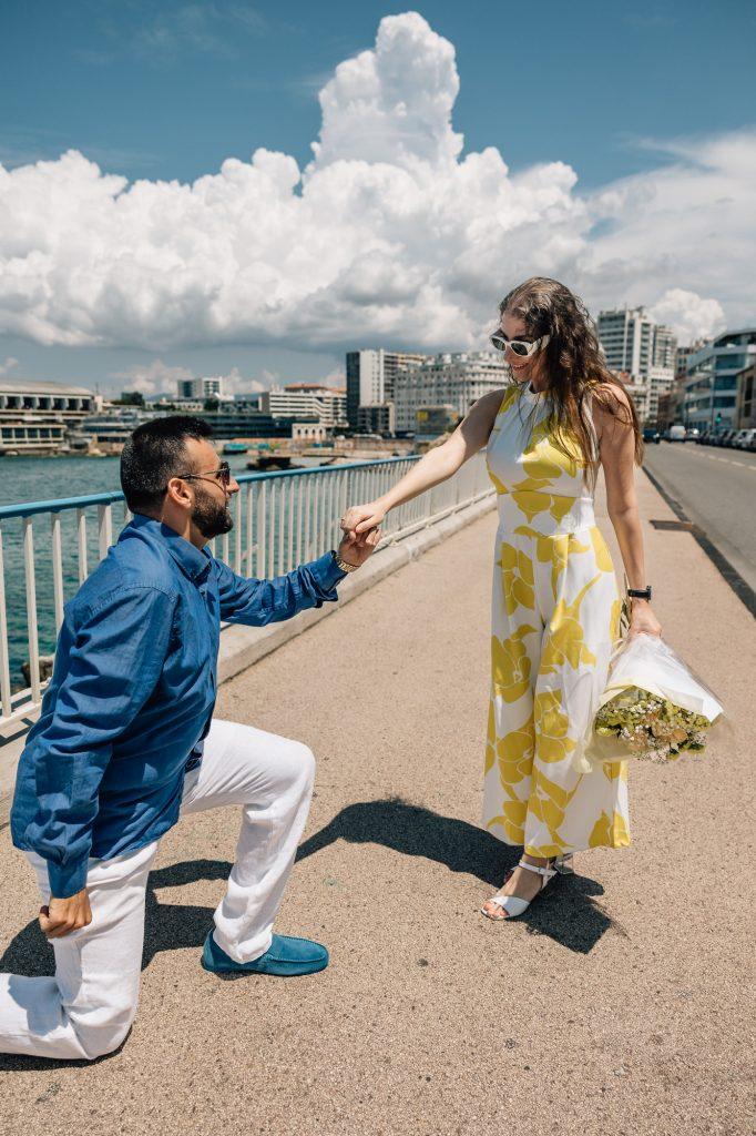 Demande en fiançailles surprise lors d'une séance photo de couple à Marseille avec la vue sur la mer. L'homme est à genou devant sa partenaire.