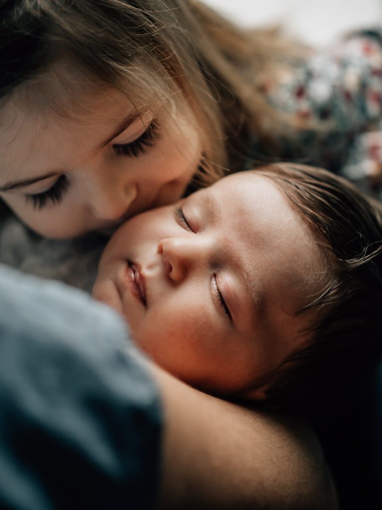 grande soeur embrassant son petit frère qui vient de naître lors d'une séance photo lifestyle à domicile