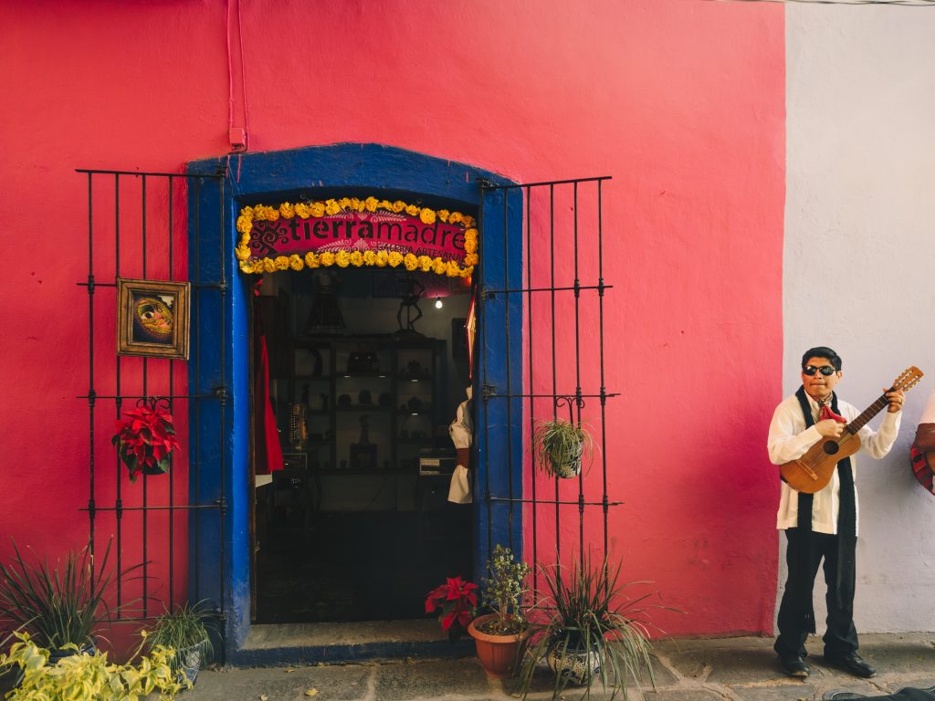 Scène de vie au Mexique : un guitariste joue près d'une porte bleue et devant un mur rose à Puebla