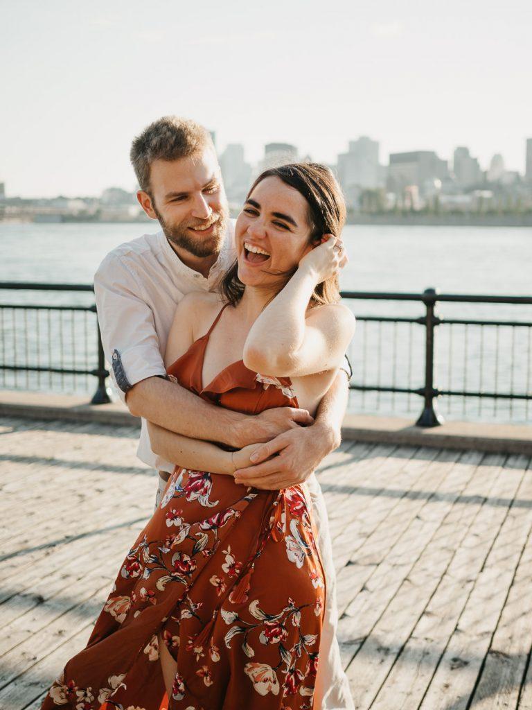 Couple d'amoureux heureux qui s'enlace face au fleuve au coucher de soleil lors d'une séance photo de couple