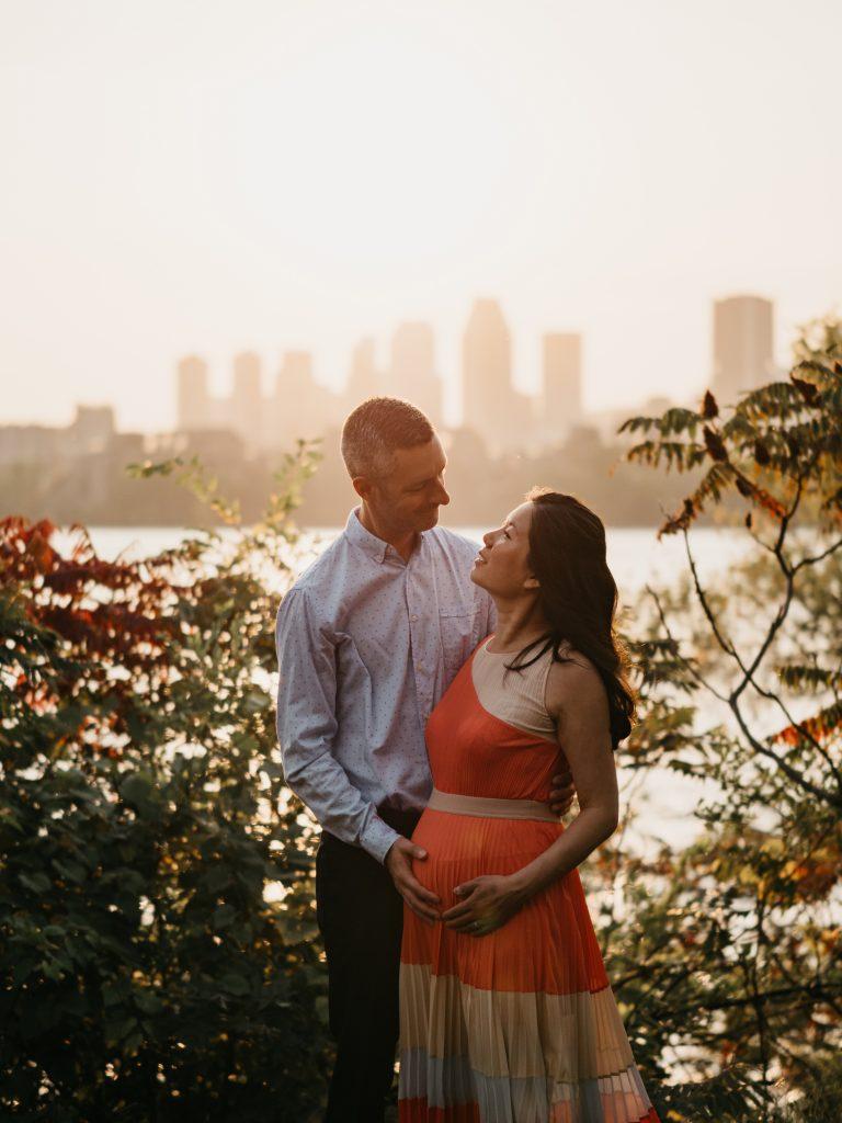 couple d'amoureux se regardant et caressant le ventre rond de la future maman au coucher de soleil lors d'un shooting photo grossesse lifestyle en extérieur