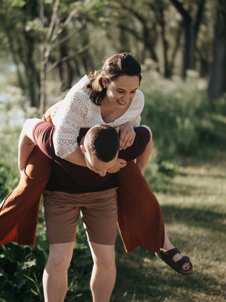 moment de complicité de couple : La femme saute sur le dos de son compagnon lors d'une séance photo engagement lifestyle dans un parc à Marseille