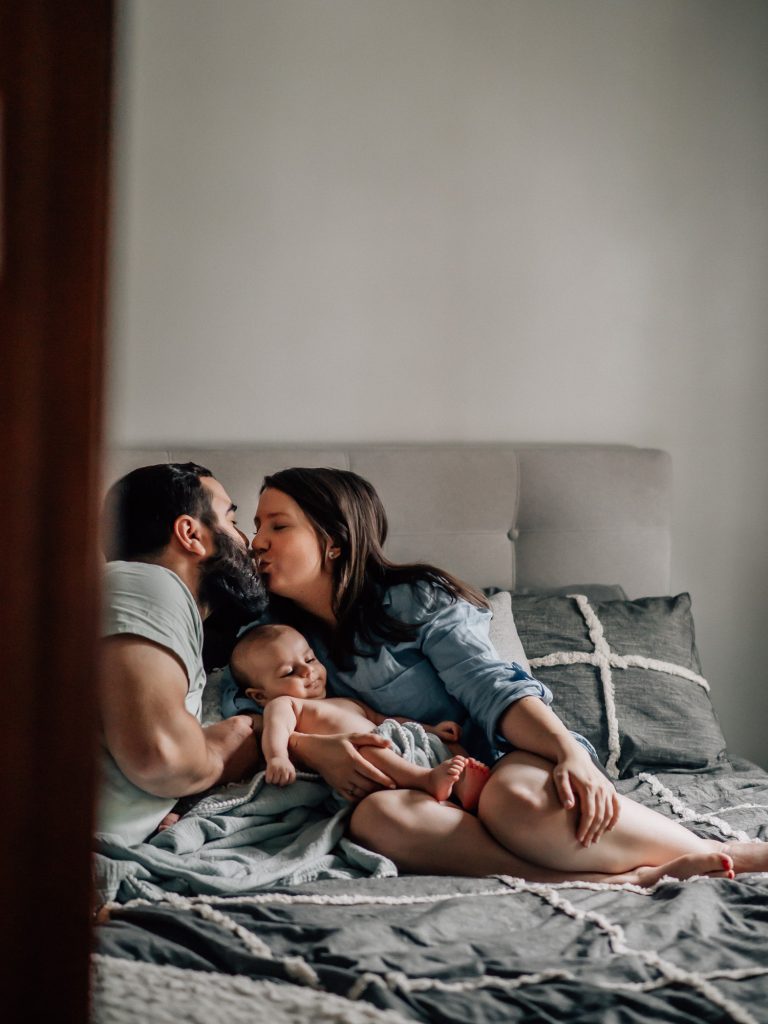 parents heureux et amoureux s'embrassent en tentant bébé dans les bras après la naissance de leur bébé lors d'un shooting photo nouveau-né lifestyle à la maison à Marseille