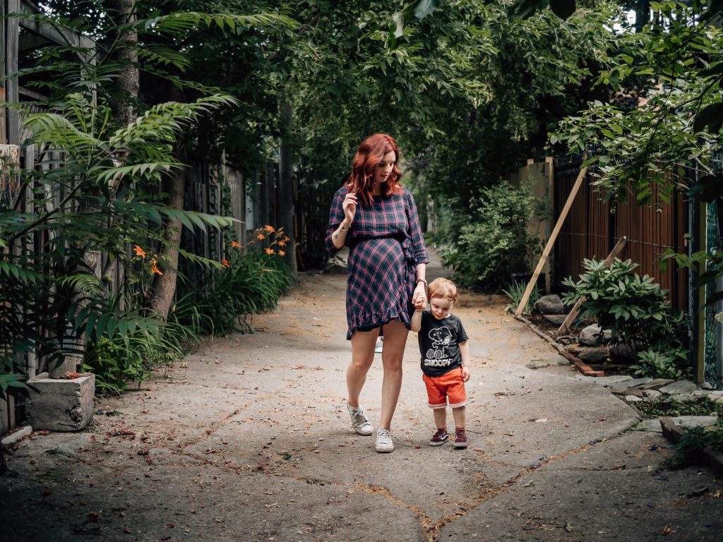 maman enceinte marche en tenant la main à son petit garçon dans une superbe ruelle arborée lors d'un shooting photo de grossesse en extérieur à Marseille