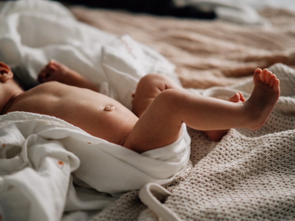 Bébé allongé sur un lit avec les jambes en mouvement lors d’une séance photo naissance à domicile