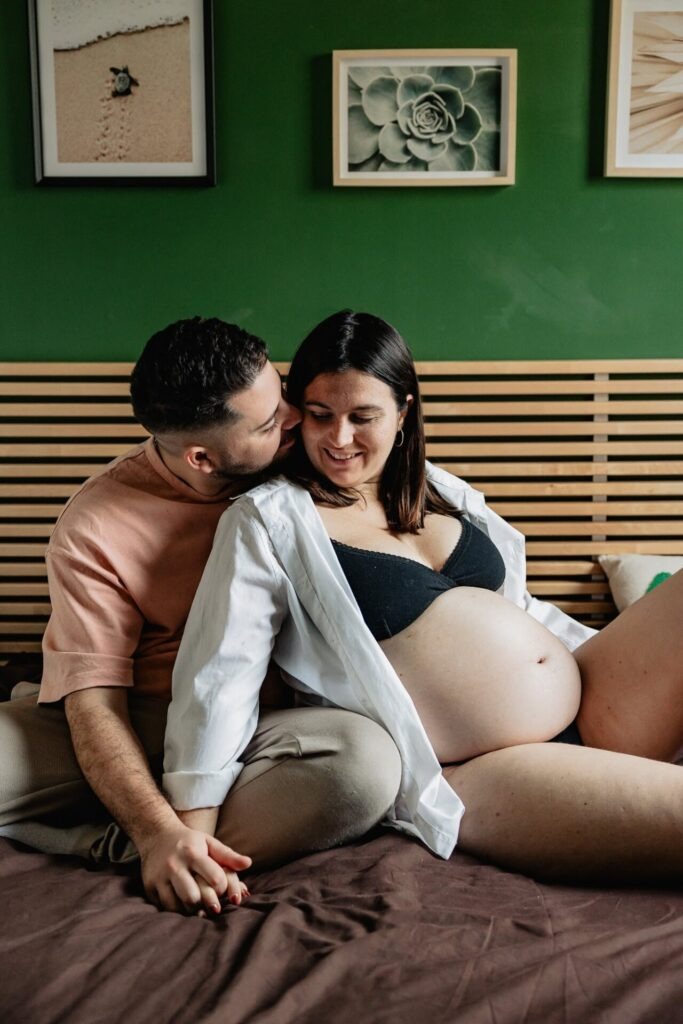 Couple assis sur leur lit lors d’une séance photo grossesse à domicile à Marseille