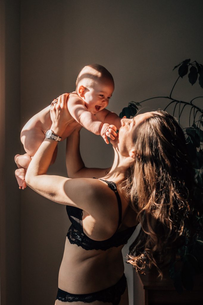 Maman levant son nouveau-né dans la lumière lors d’une séance photo bébé à domicile à Aix-en-Provence