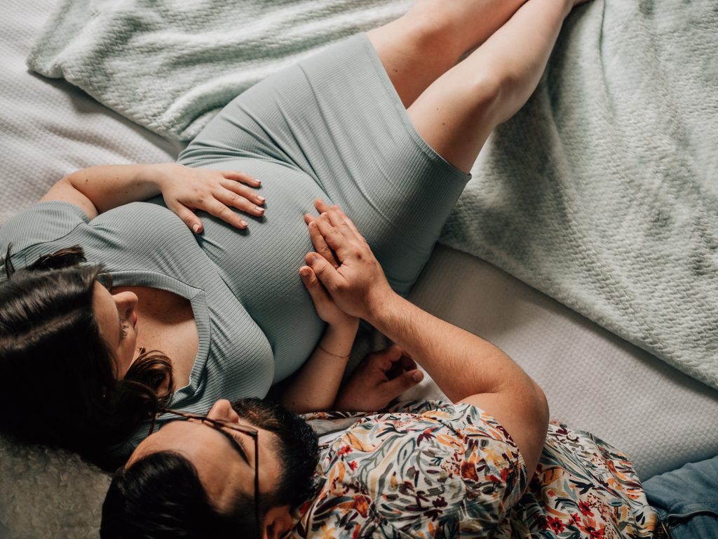 couple de futurs parents allongés sur le lit caressant le ventre de la future maman lors d'une séance photo de grossesse à domicile à marseille