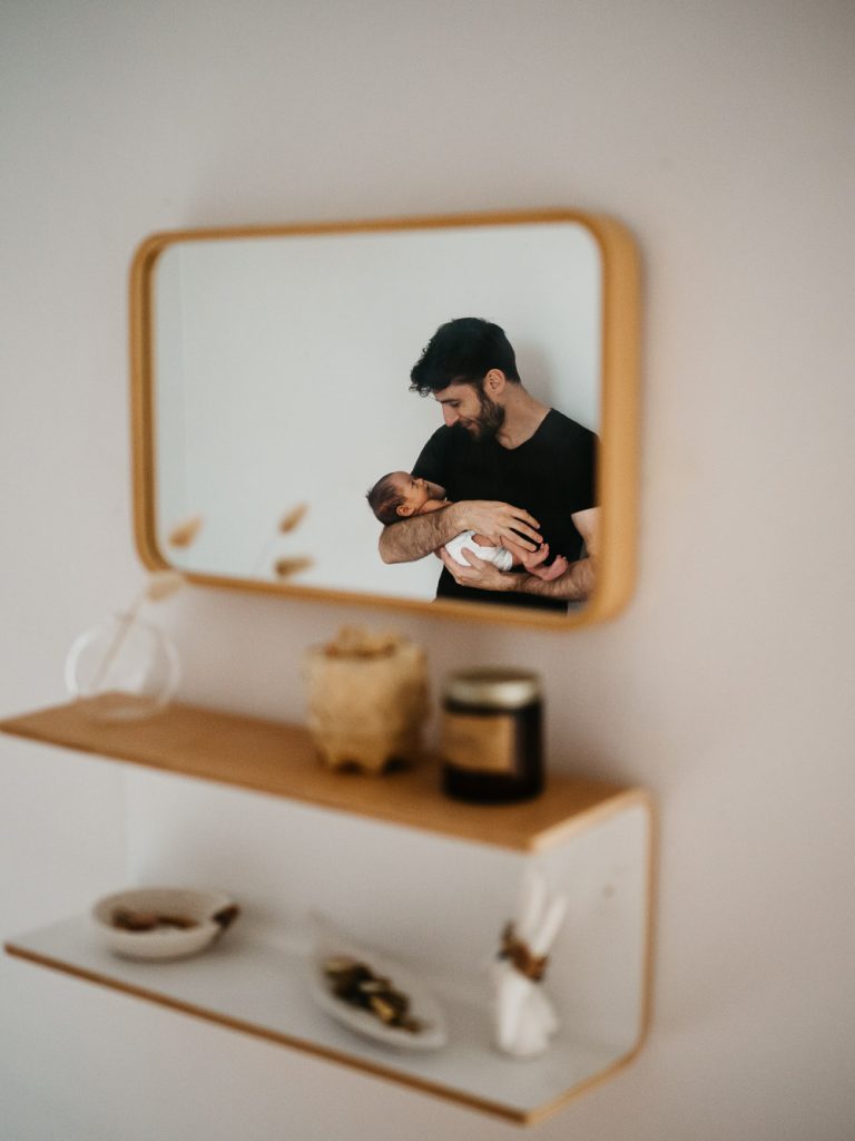 reflet dans le miroir d'un tendre portrait d'un père berçant son bébé lors d'un shooting photo famille dans la chambre d'enfant à Marseille
