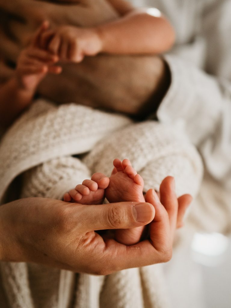 pieds de nouveau-né dans la main de son papa lors d'un shooting photo lifestyle à domicile
