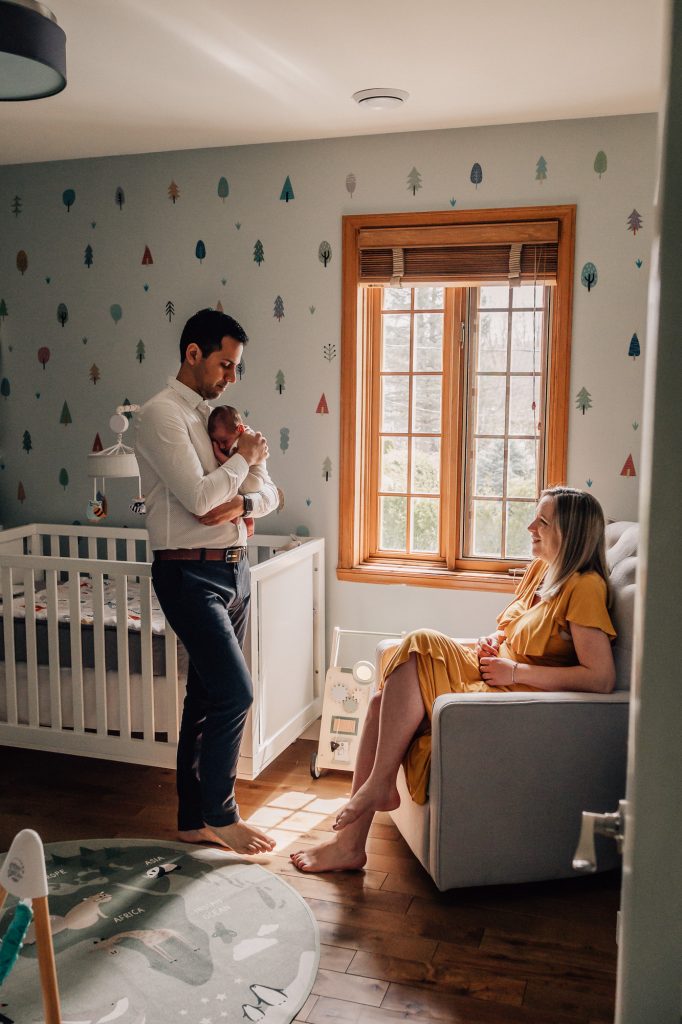 papa berce bébé dans ses bras avec la maman assise à ses côtés dans la chambre du bébé lors d'une session photo à la maison