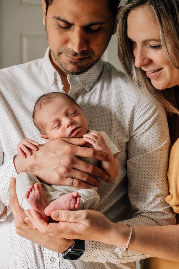 magnifique portrait de famille avec le nouveau-né entouré de ses parents le portant dans les bras lors d'une séance nouveau-né à domicile