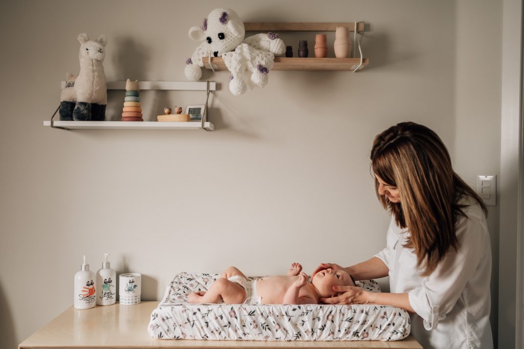maman s'occupant de son bébé sur la table à langer dans la chambre d'enfant lors d'une séance photo nouveau-né à domicile à Marseille