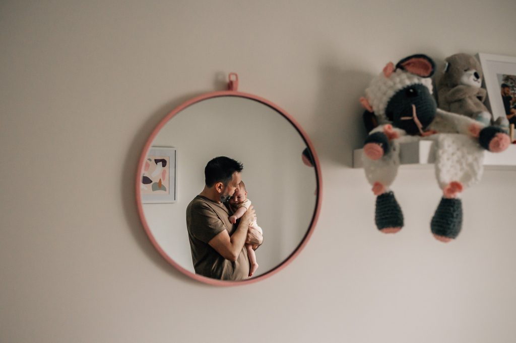 reflet dans le miroir d'un tendre portrait d'un père berçant son bébé lors d'un shooting photo famille dans la chambre d'enfant à Marseille