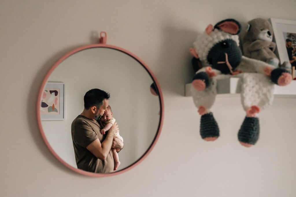 reflet dans le miroir d'un tendre portrait d'un père berçant son bébé lors d'un shooting photo famille dans la chambre d'enfant à Marseille