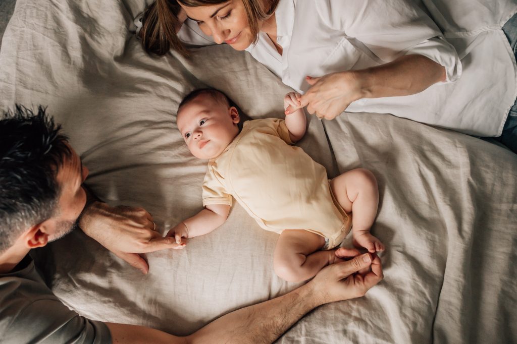 scène de vie quotidienne de nouveaux parents avec leur nouveau-né sur le lit familial lors d'un shooting photo bébé à la maison à Marseille