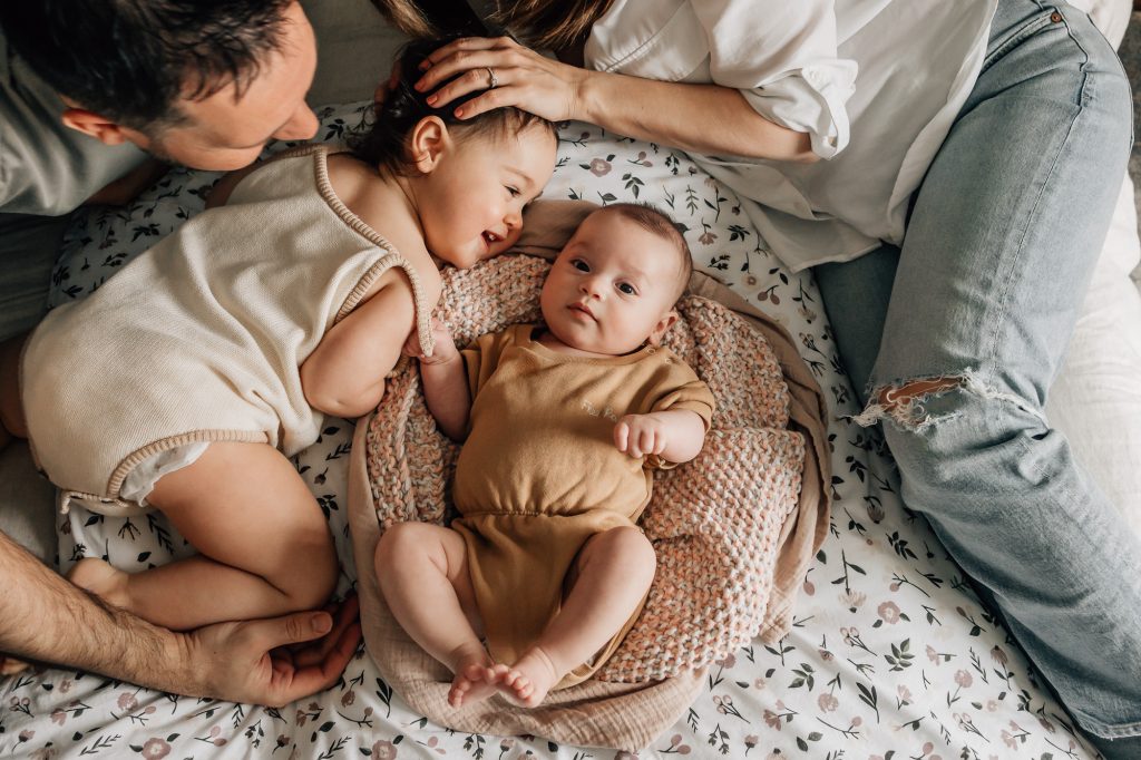 moment de tendresse et de bonheur avec les parents regardant tendrement leurs deux bébés filles jouer sur le lit lors d'une séance photo nouveau-né à Marseille