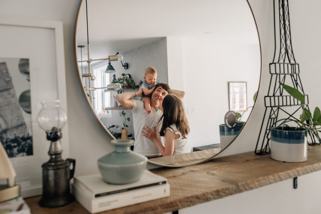 portfolio de séance photo de famille à domicile à Marseille : reflet dans un miroir d'un bébé sur les épaules de son papa