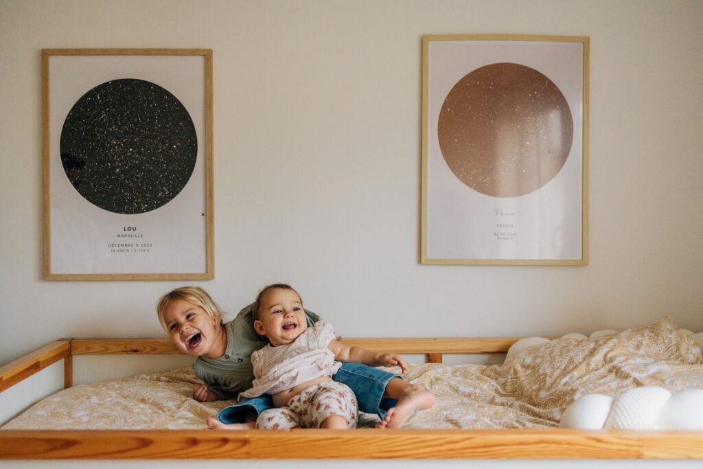 Deux enfants riant sur un lit lors d'une séance photo de famille à domicile