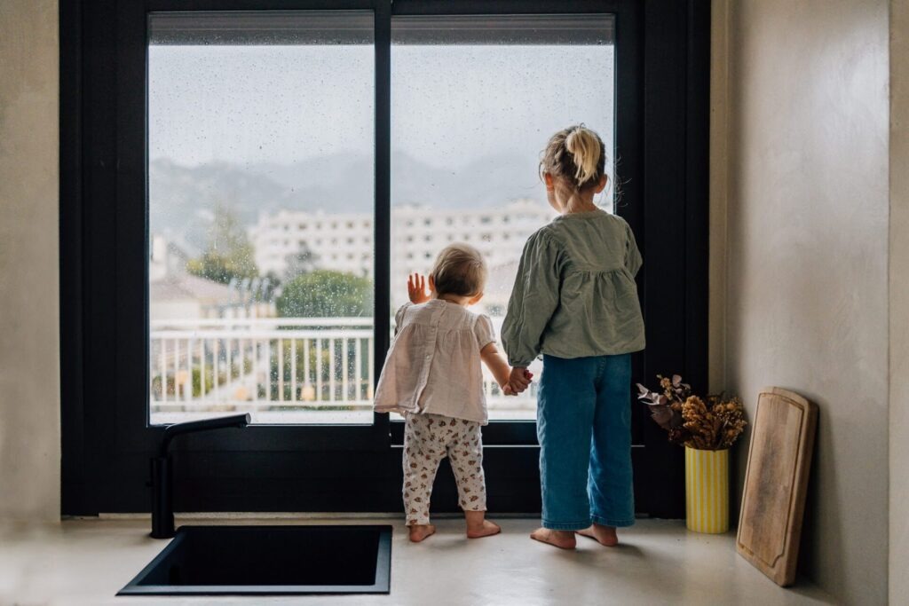 Deux enfants regardant la pluie par la fenêtre lors d'une séance photo de famille à domicile à Marseille 13009