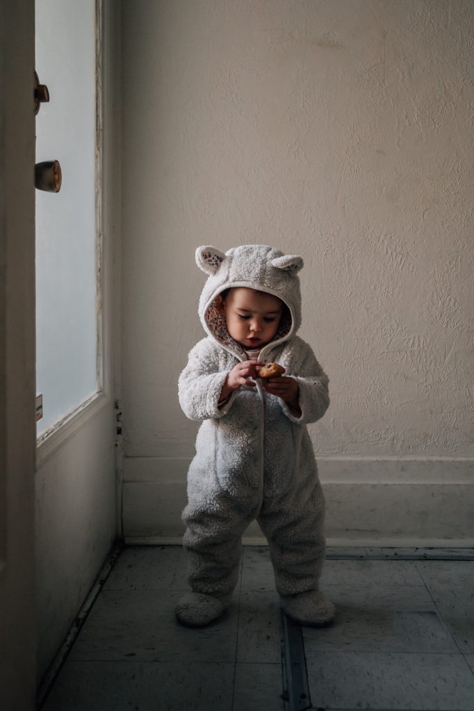 petite fille en tenue de lapin en guise de manteau d'hiver mange un biscuit au chocolat lors d'un reportage photo à la maison