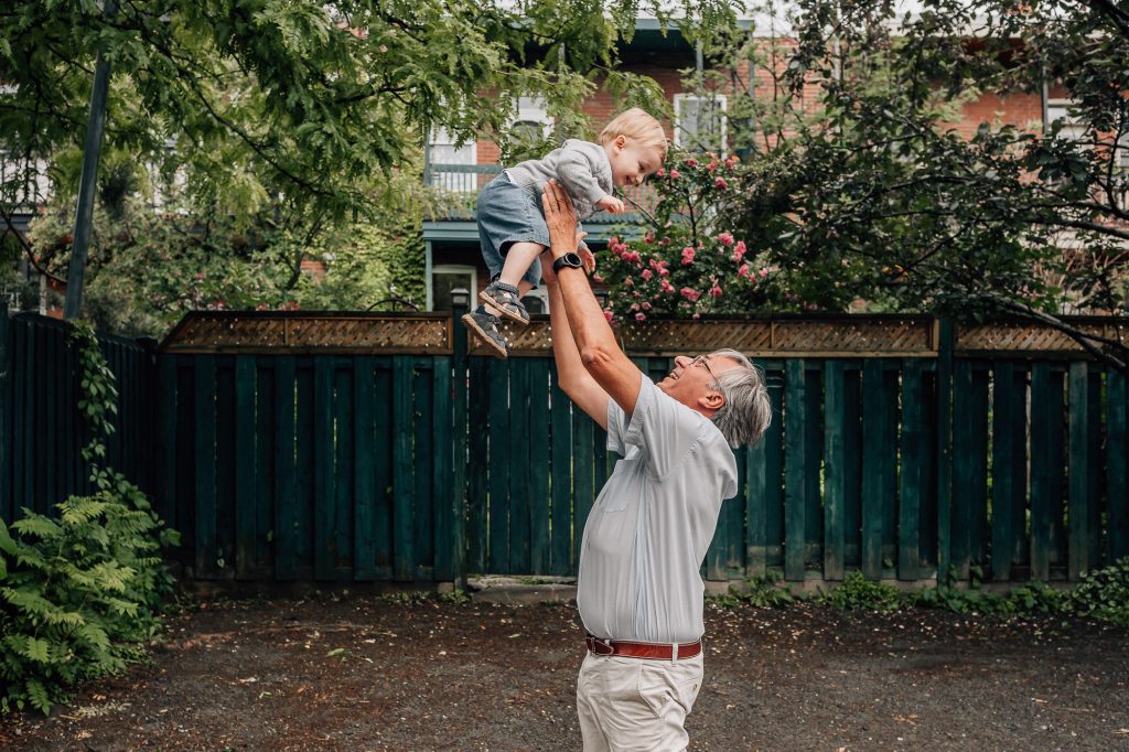 papi heureux qui joue avec son petit-fils en le lançant dans les airs lors d'une séance photo lifestyle famille nombreuse à Marseille