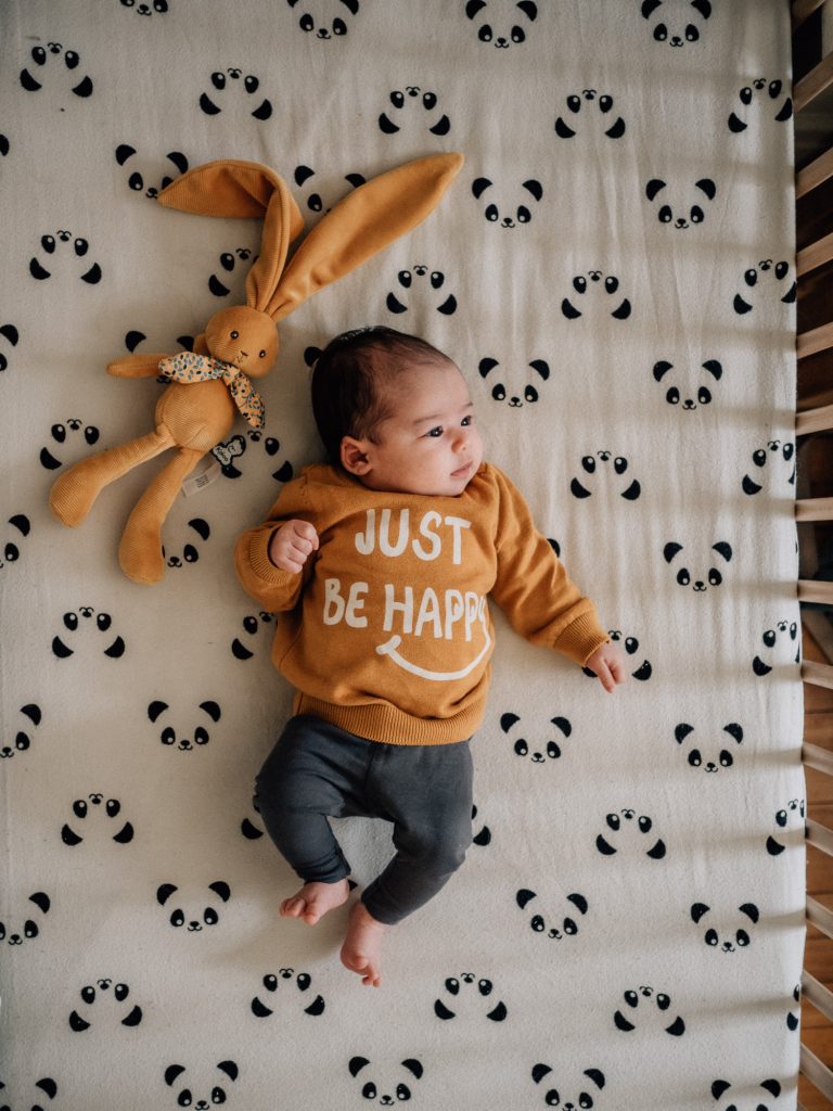 portrait pour un faire-part de naissance d'un nouveau-né dans son lit avec une peluche et un pull "Just be happy" de la marque Vertbaudet lors d'une séance photo nouveau-né à Marseille