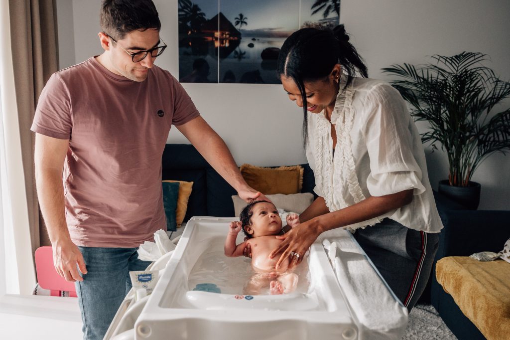 nouveau-né prend son bain entouré de ses parents lors d'un shooting photo lifestyle à domicile