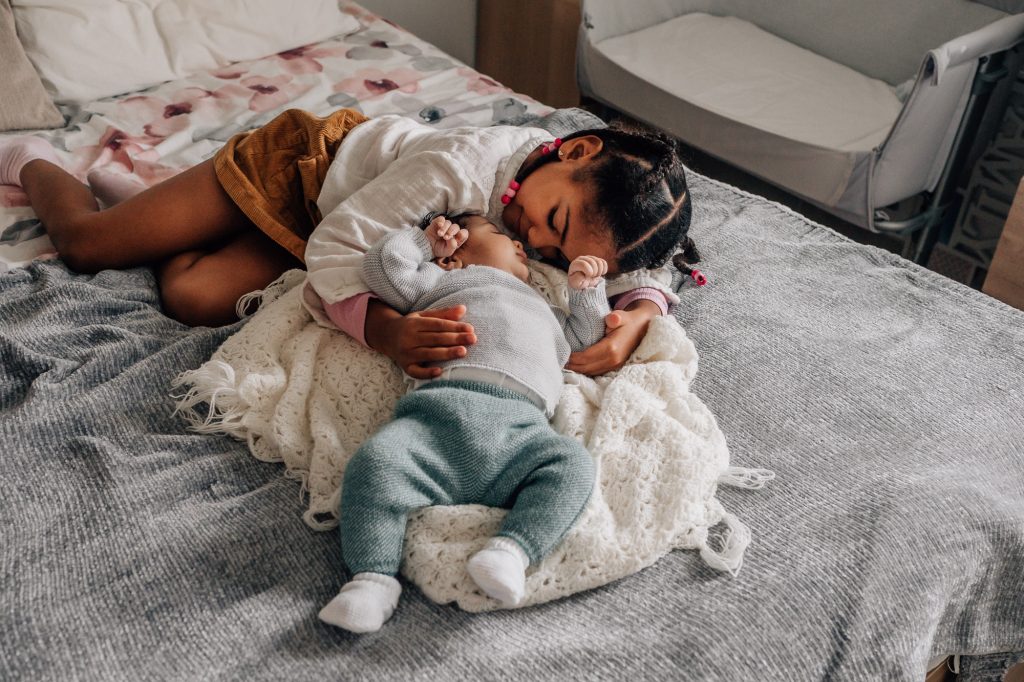 grande soeur câlinant son petit frère d'un mois lors d'une séance photo bébé lifestyle à domicile à Marseille