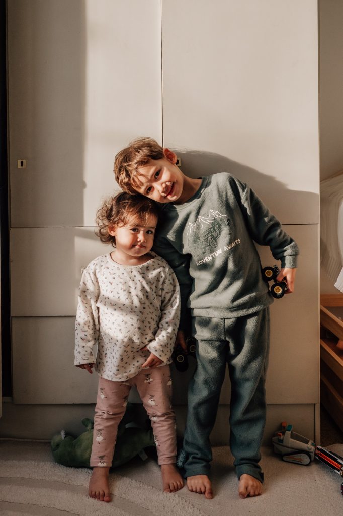 portrait de deux jeunes enfants : un frère et sa soeur en pyjama dans un rayon de soleil dans leur chambre lors d'un reportage photo famille à la maison à Marseille