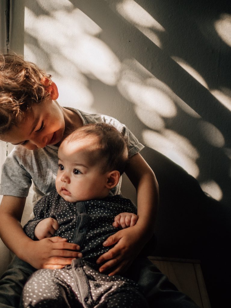 portrait d'un grand frère avec sa petite soeur de quelques mois dans un sublime rayon de lumière lors d'une séance photo de famille à Marseille