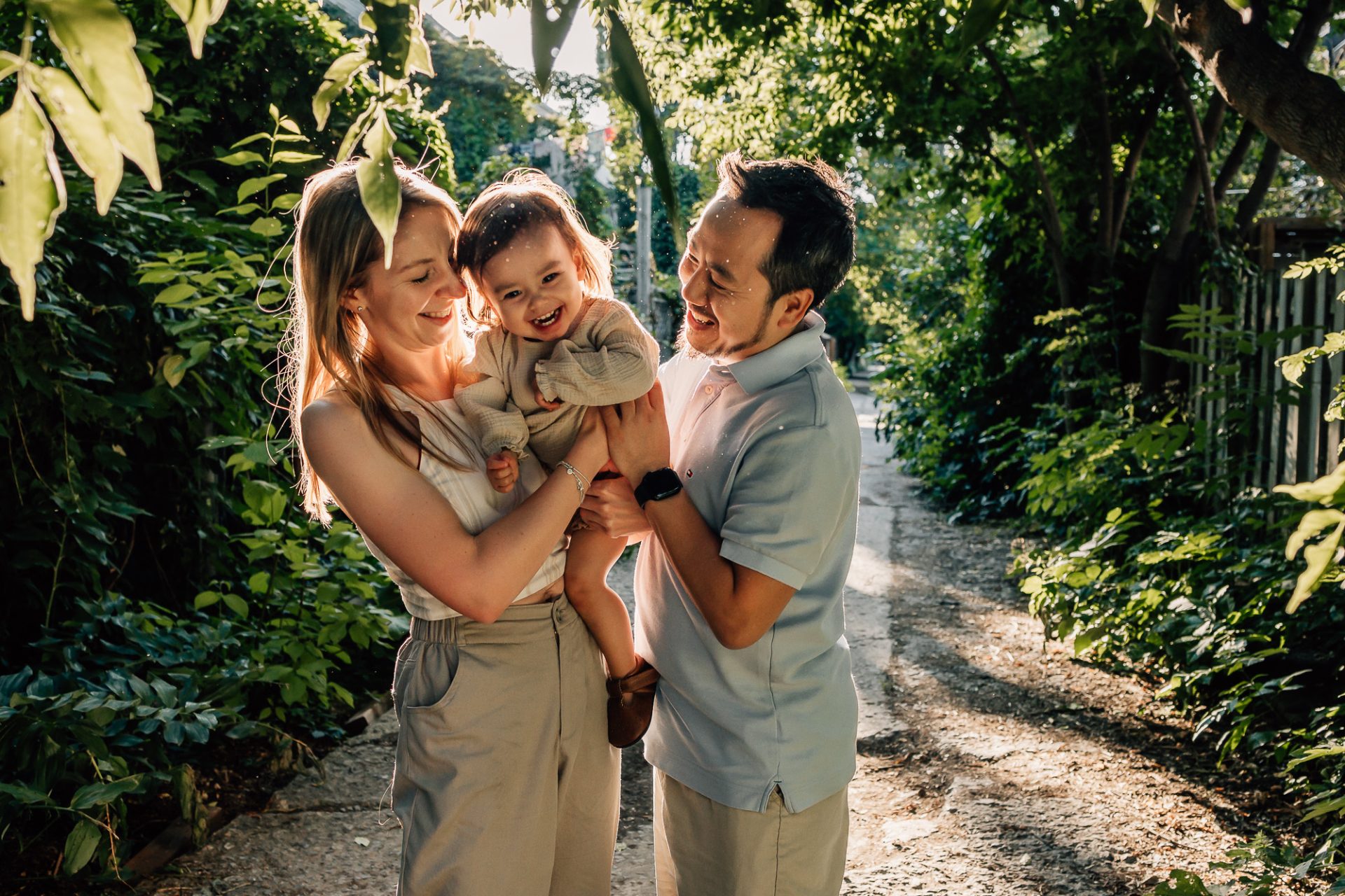 moment de joie de parents faisant des chatouilles à leur petite fille qui rit aux éclats dans une belle ruelle de nature lors d'une séance photo famille à Marseille