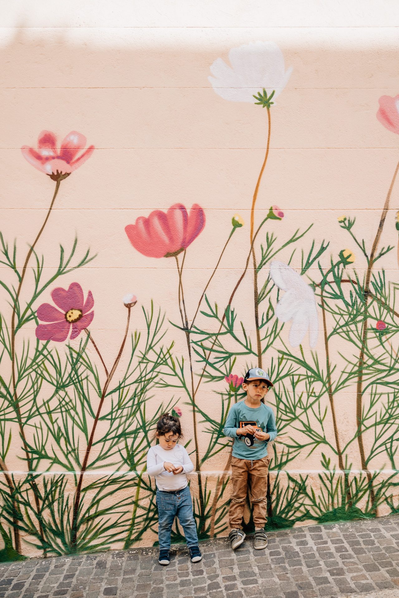 un frère et une soeur devant un mur avec une fresque murale fleurie lors d'un shooting photo famille à Marseille dans le quartier du Panier