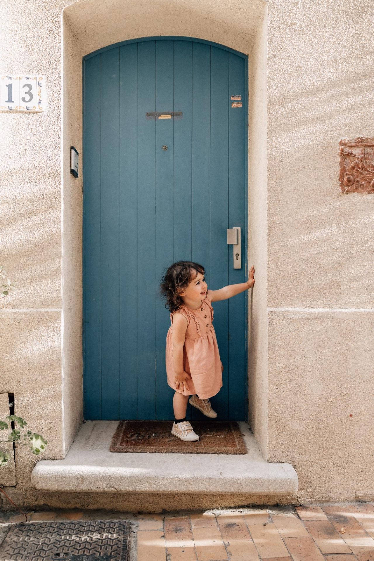 petite fille joue à cache-cache devant une porte bleue dans les ruelles de Cassis, petit village provençal lors d'une séance photo en famille